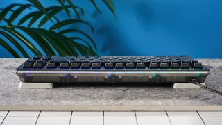 The Wooting 80HE in Ghost PCR case with black keycaps, on a stone surface with a blue background.