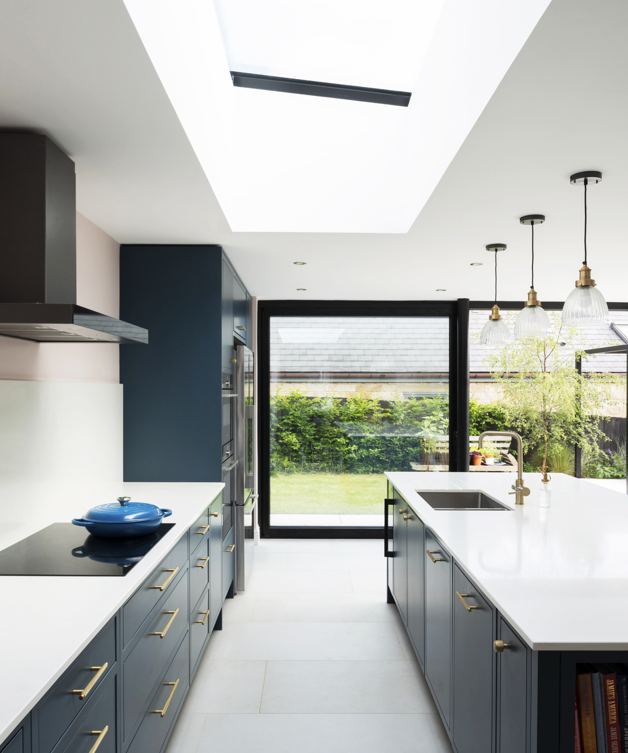 Kitchen with blue cabinet doors and a island in the middle of the room. A rooflight is installed in the ceiling and a large patio door overlooking the garden is directly in the background