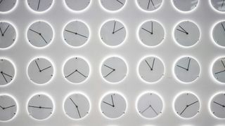 A series of white analog clocks against a gray background, their faces showing various different times.