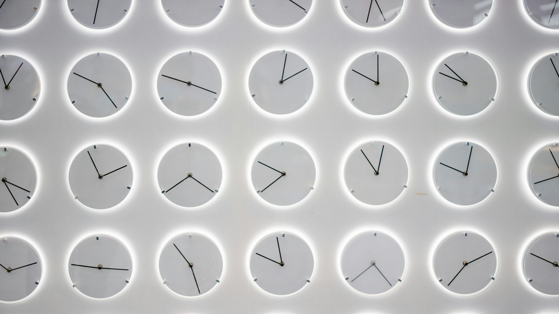 A series of white analog clocks against a gray background, their faces showing various different times.