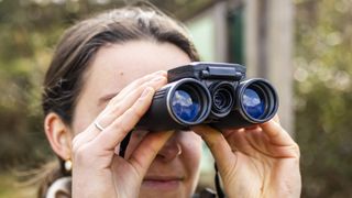 A female photographer holds the Camonity 5M 2" LCD 32GB Digital Binoculars in her hands in a sunny field