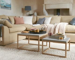 Square nesting tables in mixed materials styled with tray and stack of books, on chunky texture cream rug, with squishy sand sofa and assorted scatter pillows.