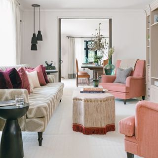 A white living room with coral pink armchairs and black pendant lights in one corner