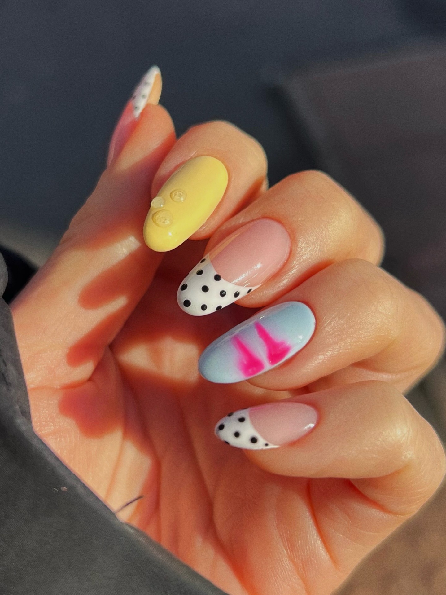 A close-up of a manicure with blue and yellow nails and black and white polka dot French tips