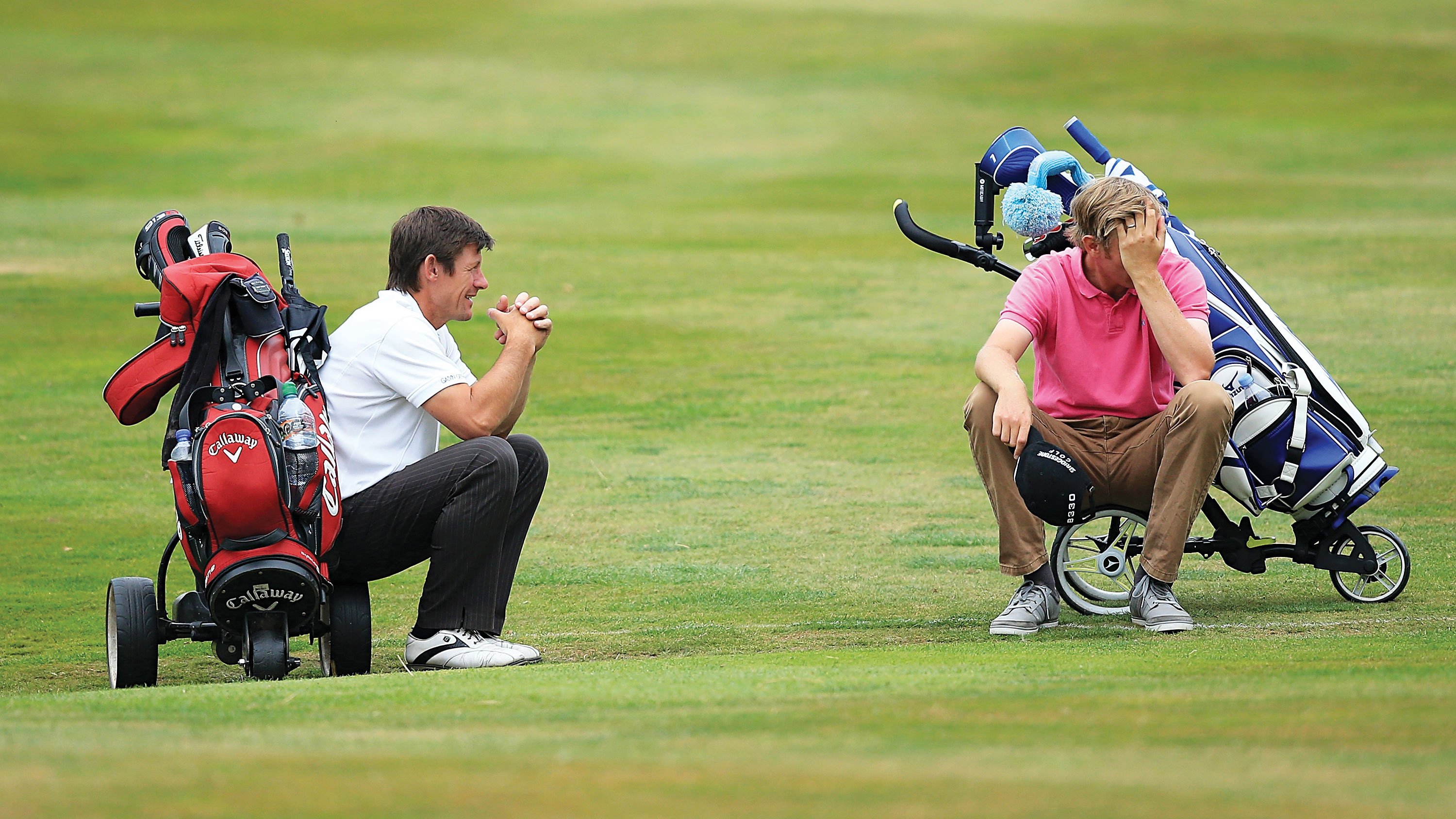 two golfers sitting on their golf bags because of slow play