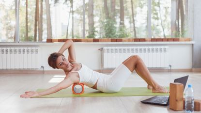 A woman using a foam roller to massage aching muscles in her back 