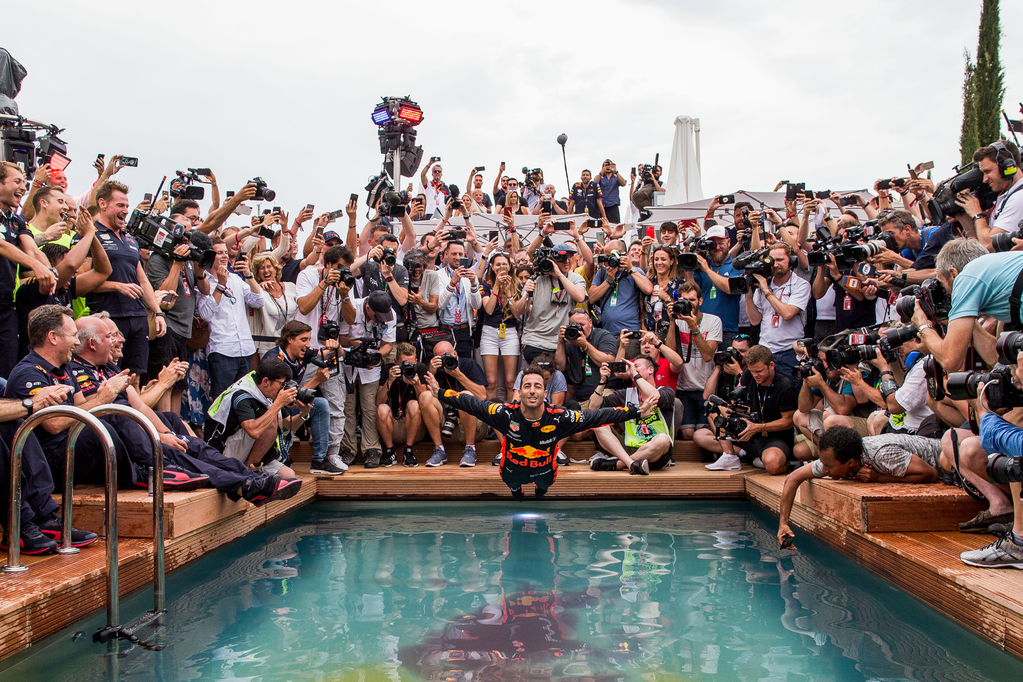 Daniel Riccardo dives into a small swimming pool, still in his race suit, surrounded by photographers 