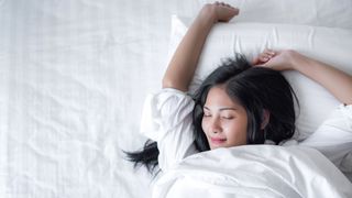 A woman sleeps happily with her arm raised on a comfortable white mattress