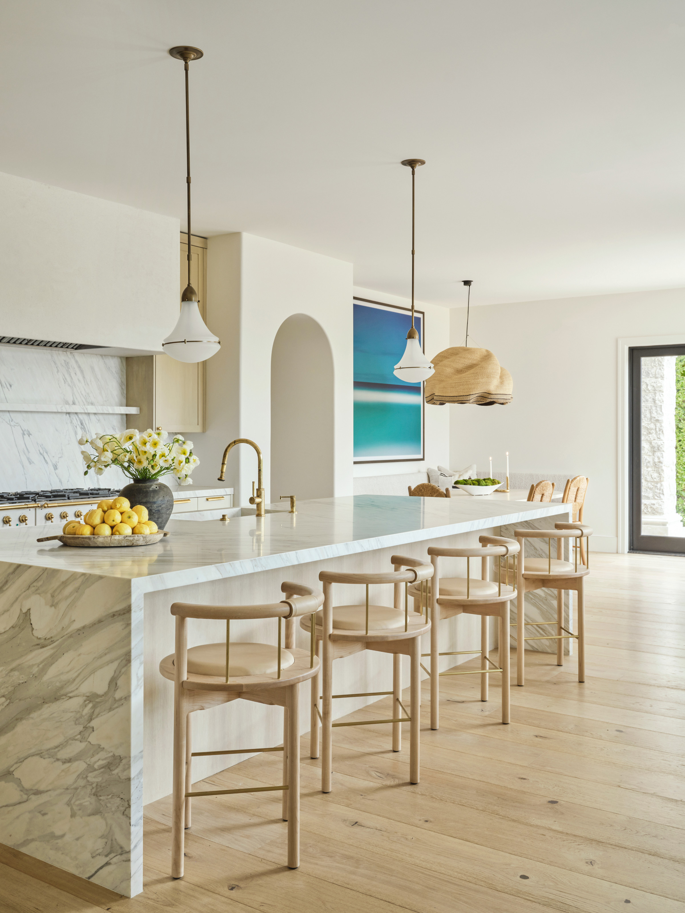 White kitchen with white marble waterfall island, pale wood bar stools and white glass pendant lights