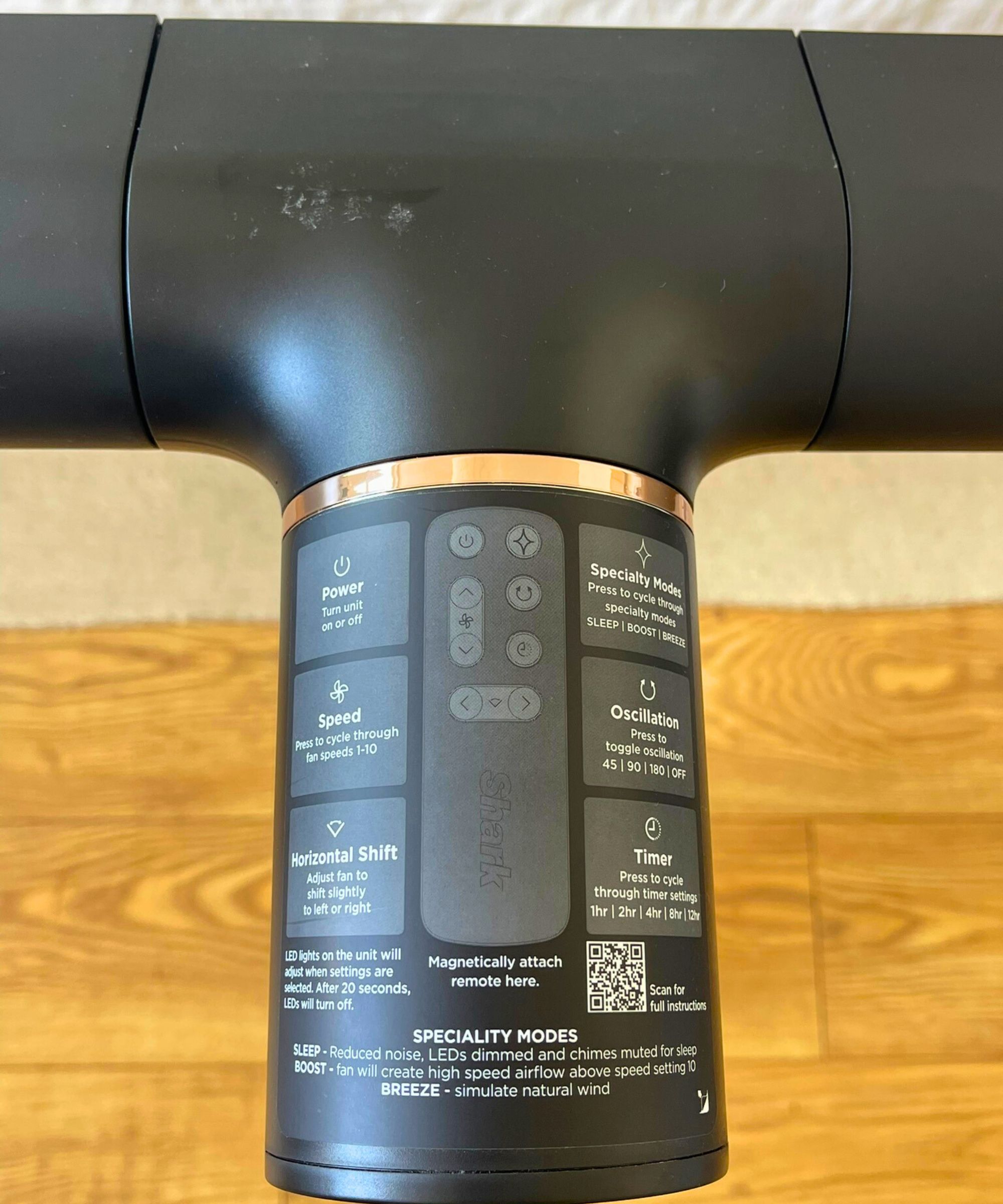 Top-down closeup of Shark TurboBlade fan with a sticker explaining the various controls, including Power, Speed, Horizontal Shift, Specialty mode, Oscillation, and Timer in Dan Fauzi's home, with wooden floor and cream rug pictured in the background.