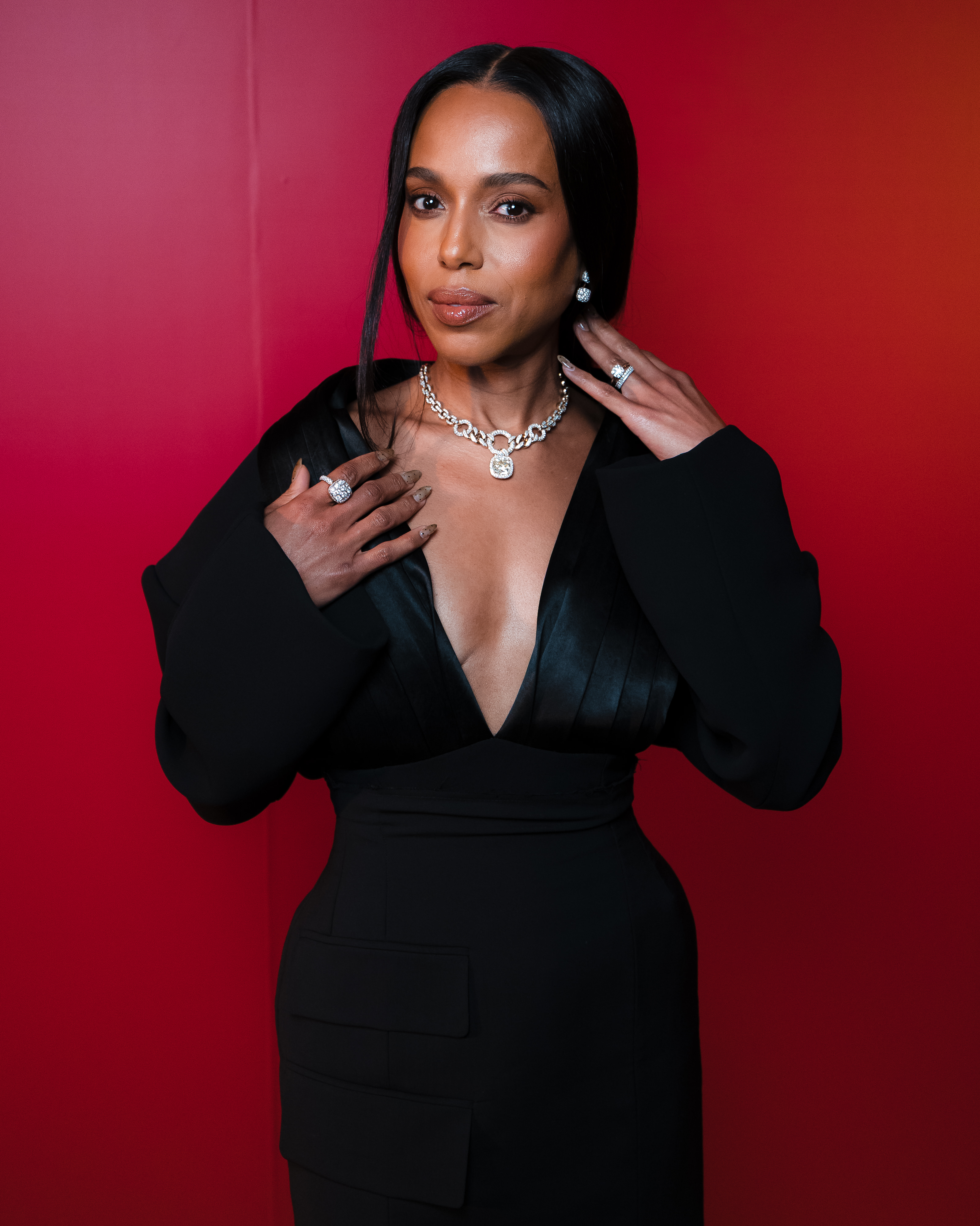 a black woman with dark hair wears a black dress and poses in front of a red background