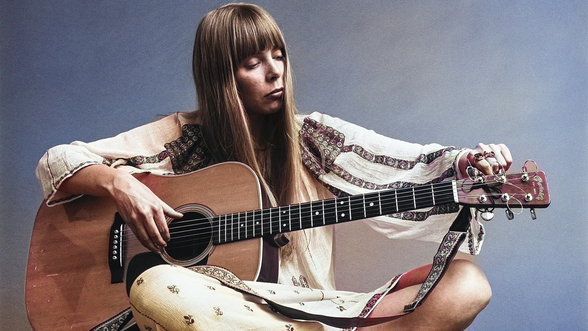 View of Canadian-American Folk musician Joni Mitchell, sitting cross-legged on the floor, as she tunes an acoustic guitar, New York, New York, November 20, 1968. The photo was taken during a shoot for Vogue magazine.