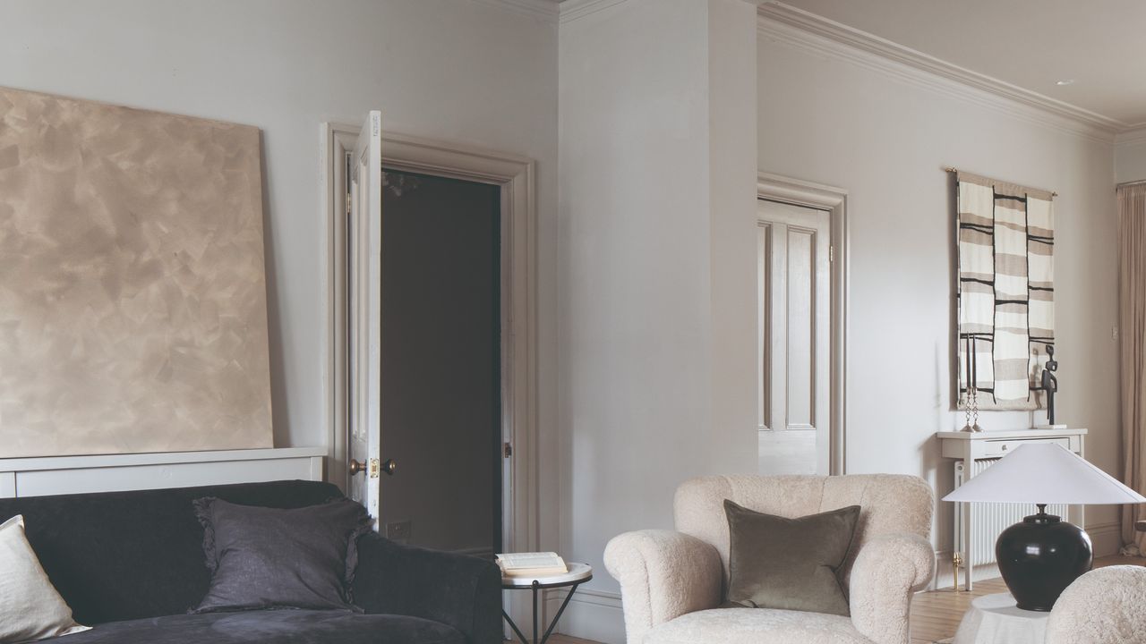 An off white-painted living room with a large abstract artwork and a black velvet sofa