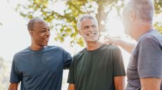 Three older man laugh and pat one another on the back in the park.
