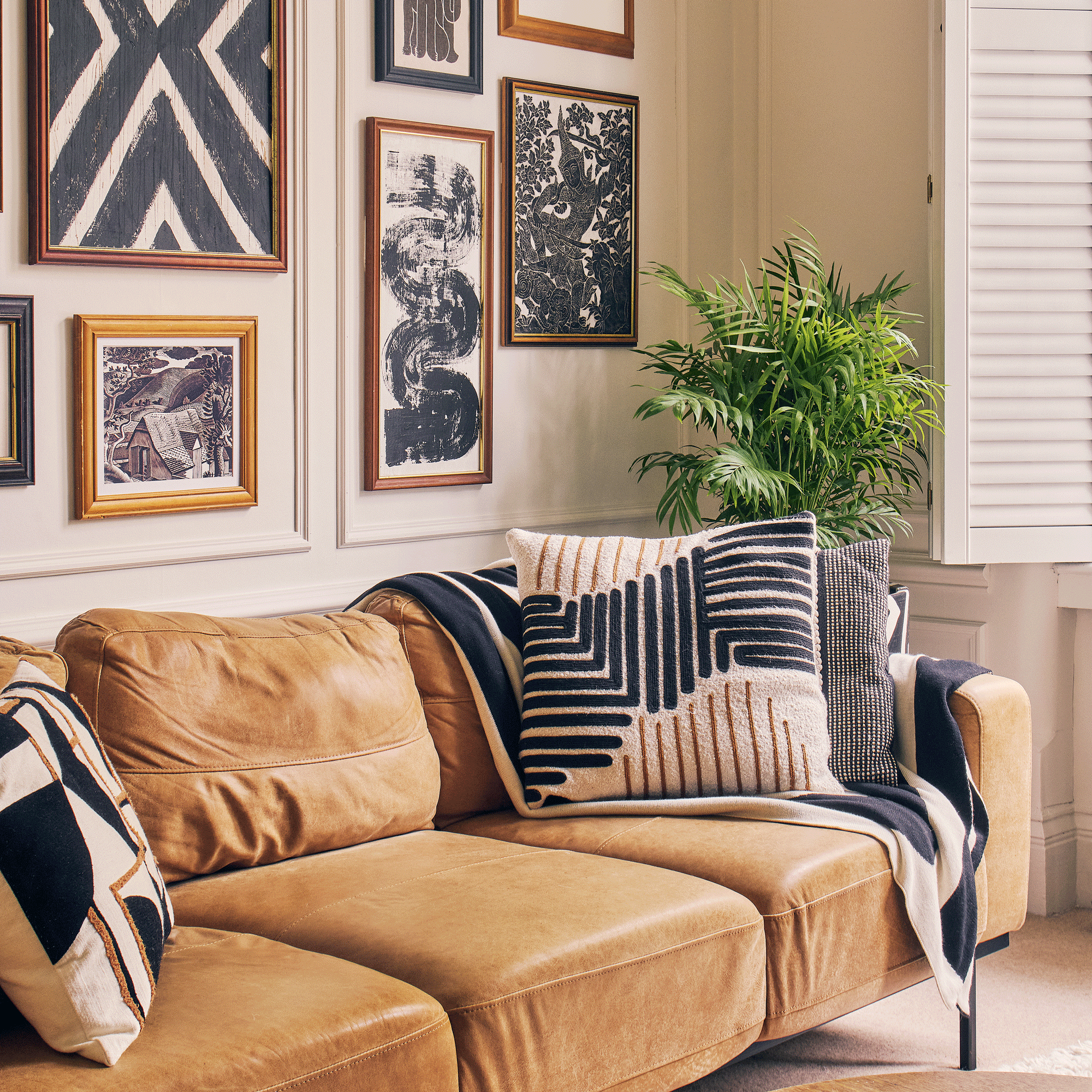 a living room with a brown leather sofa covered in graphic patterned monochrome cushions and a throw with a bold black and white gallery wall behind it