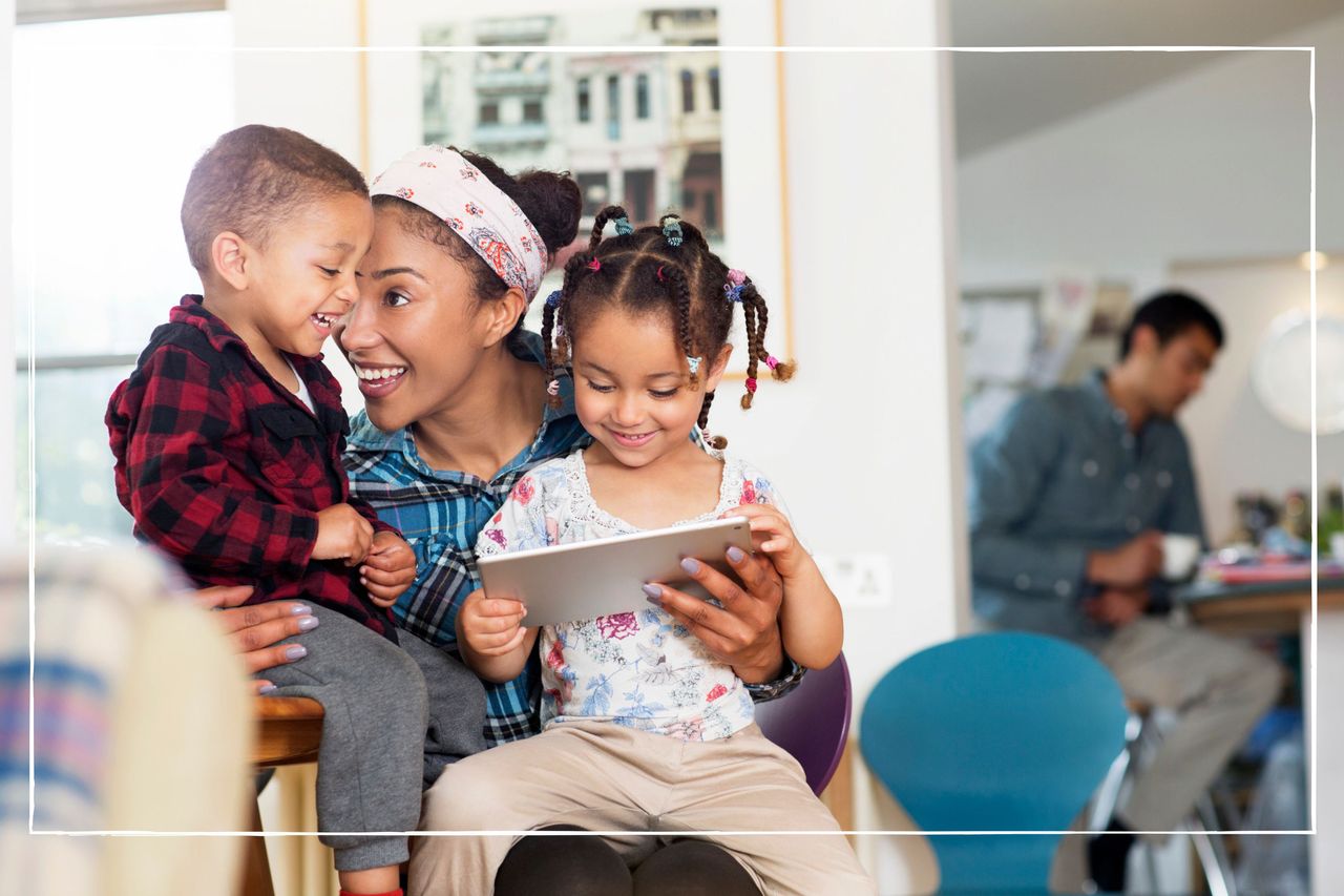 Mum holding her two children on her lap, looking at a tablet device together