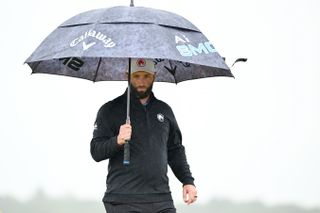 Jon Rahm walks under an umbrella