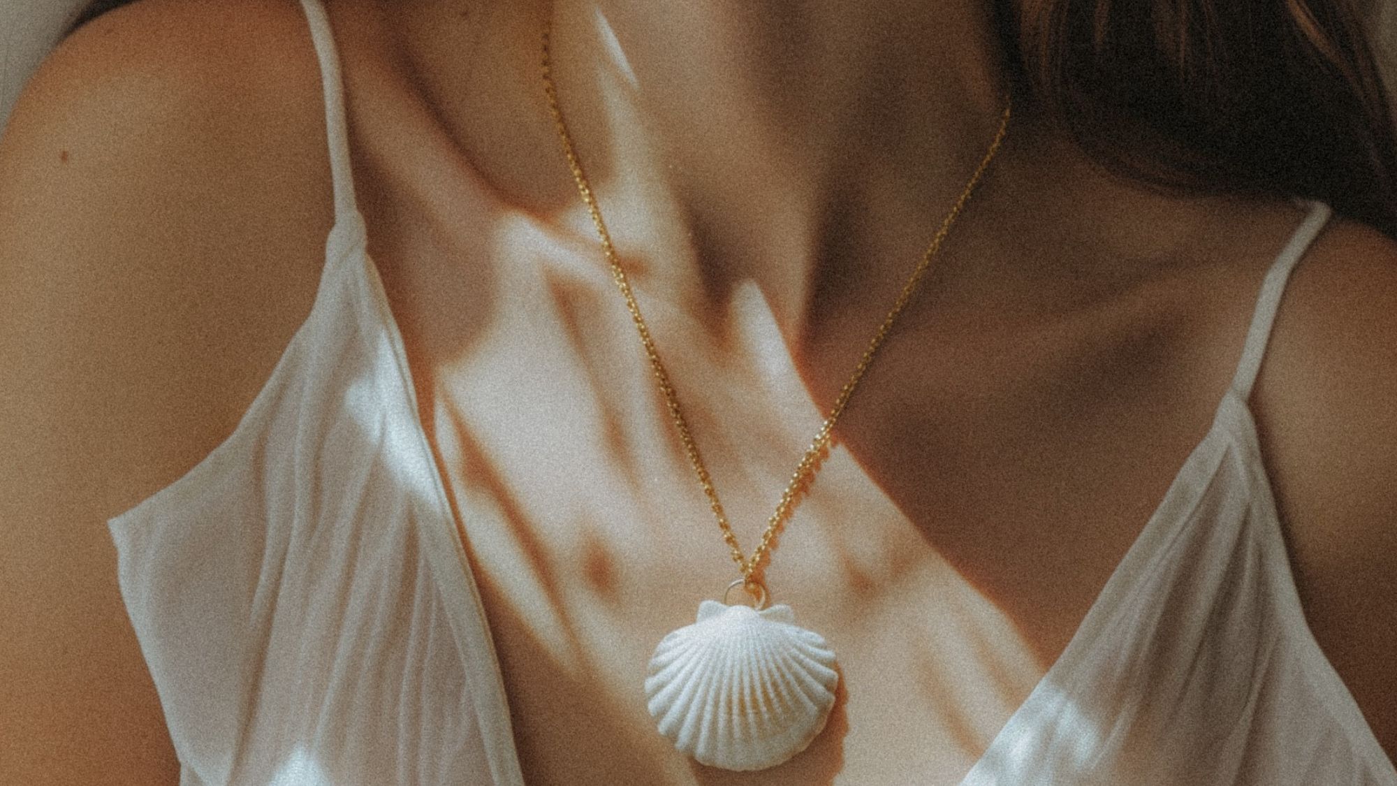 A woman's collarbones with a shell necklace and slip camisole top