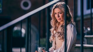 Fran (EVE MYLES) drinking coffee on some steps leading up to a house.