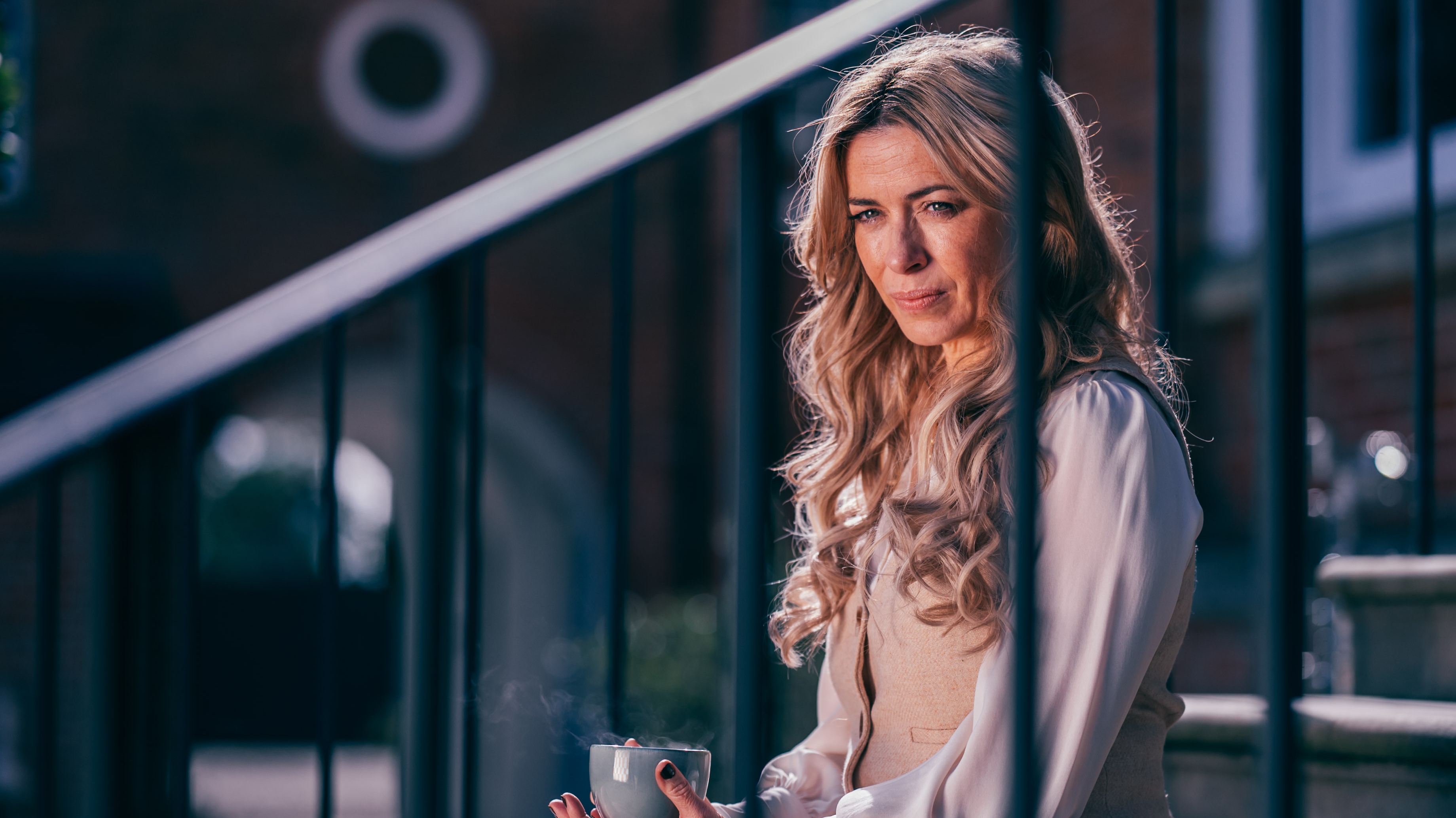 Fran (EVE MYLES) drinking coffee on some steps leading up to a house. 