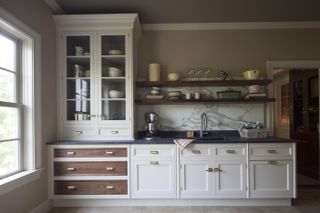 ktichen/pantry with taupe walls, off white painted cabinets, marble splash back, open shelving, glass cabinet on top of countertop