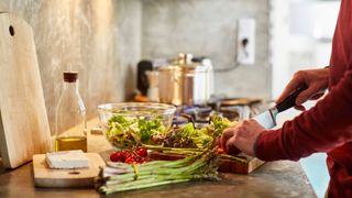 Woman putting salad into a glass bowl in the kitchen, asparagus and tomato, with olive oil for healthy fats