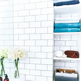 white bathroom with metro tiles and shelves with towels on