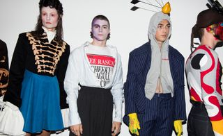 Models wearing various headwear, suit outfits, face paint
