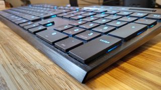 A black Corsair K100 Air Wireless keyboard on a wooden table