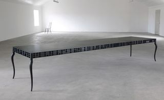 View of the 'Foundrie Table' by Gregor Jenkin - a very long dark coloured table with a black design on the sides featuring small squares
