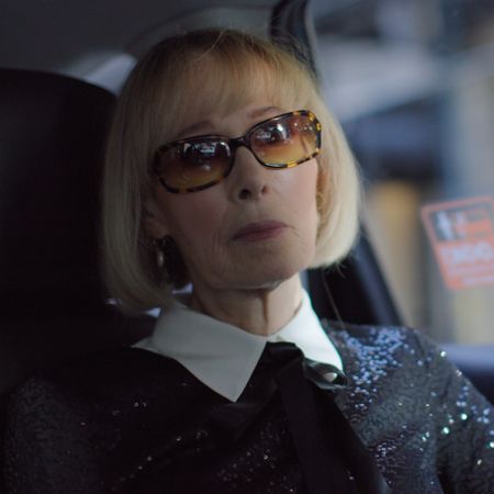 writer e. jean rides in the back of a car wearing sunglasses and a sparkly buttoned up top in a still from the documentary ask e jean