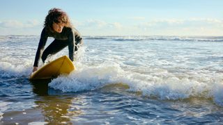 Woman wearing wetsuit riding a surfboard across waves