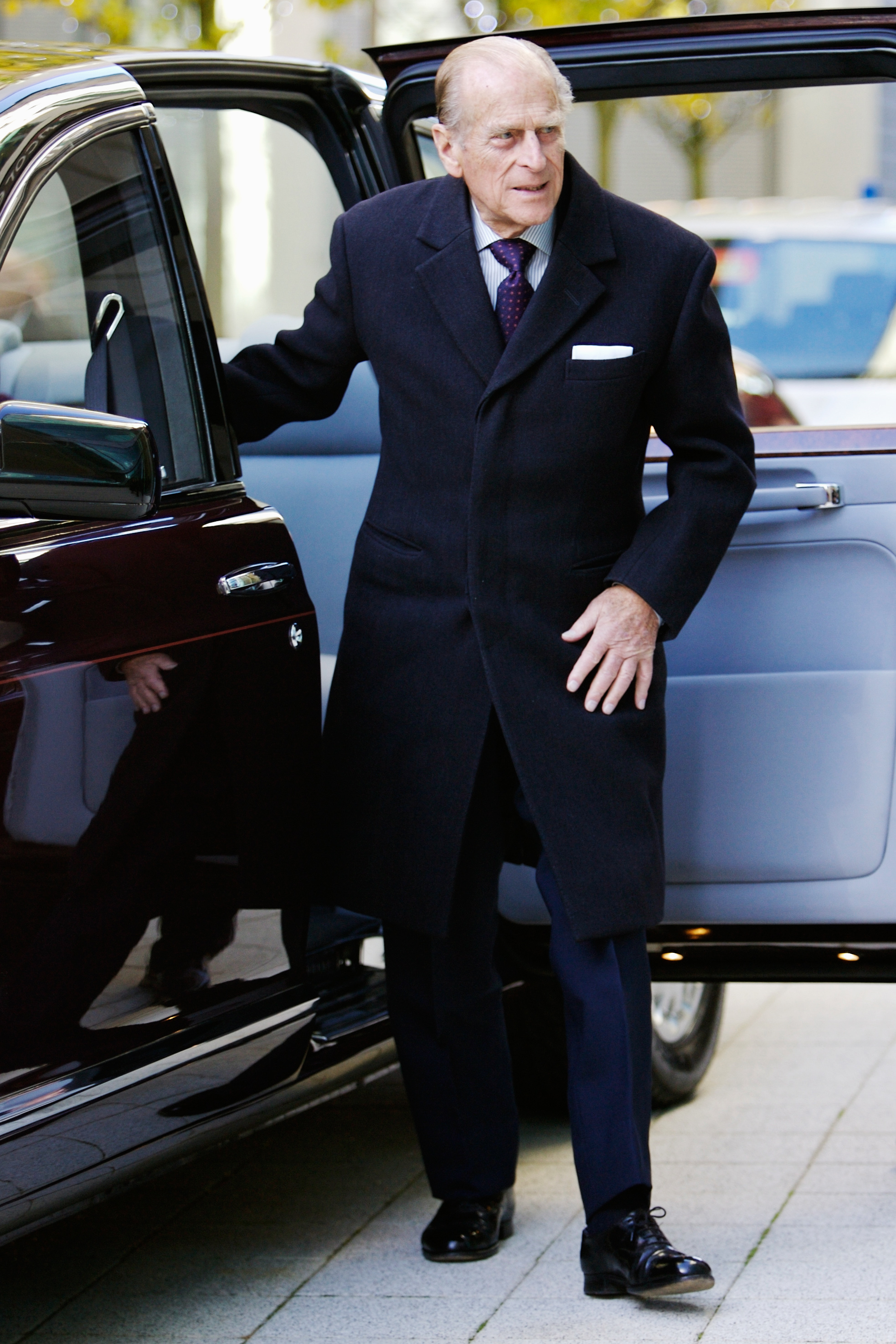 Prince Philip wearing a dark coat stepping out of a car