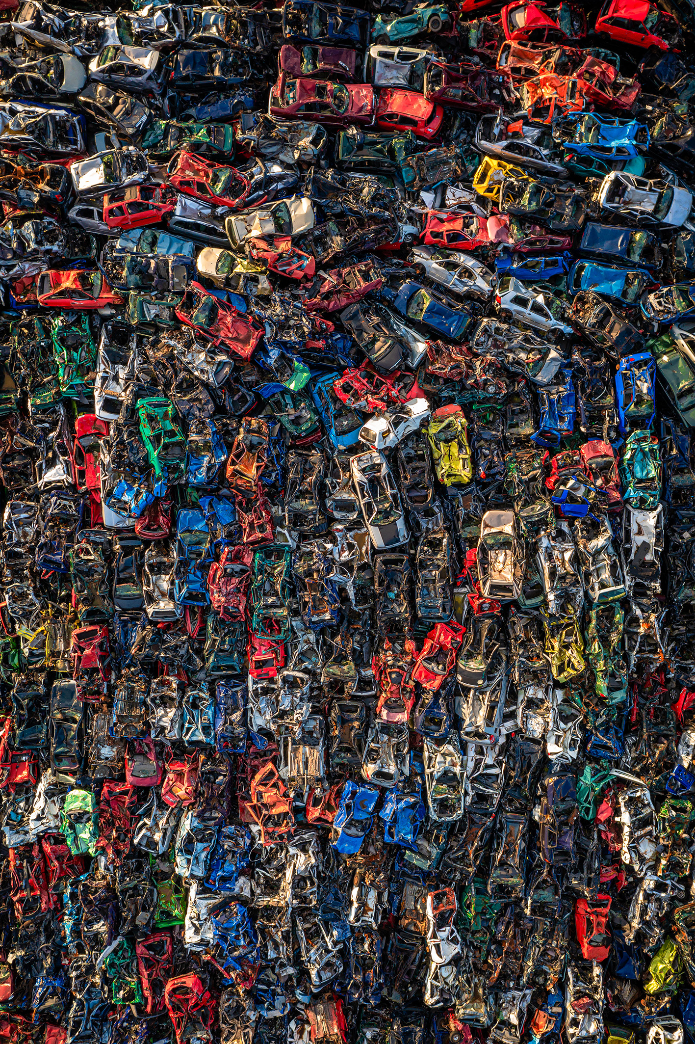 Aerial view of a junkyard filled with densely packed, crushed cars in various colors, showcasing the remnants of many vehicles
