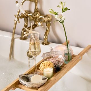 Bath tray styled with glass of bubbles, natural sponge, shells and candle.