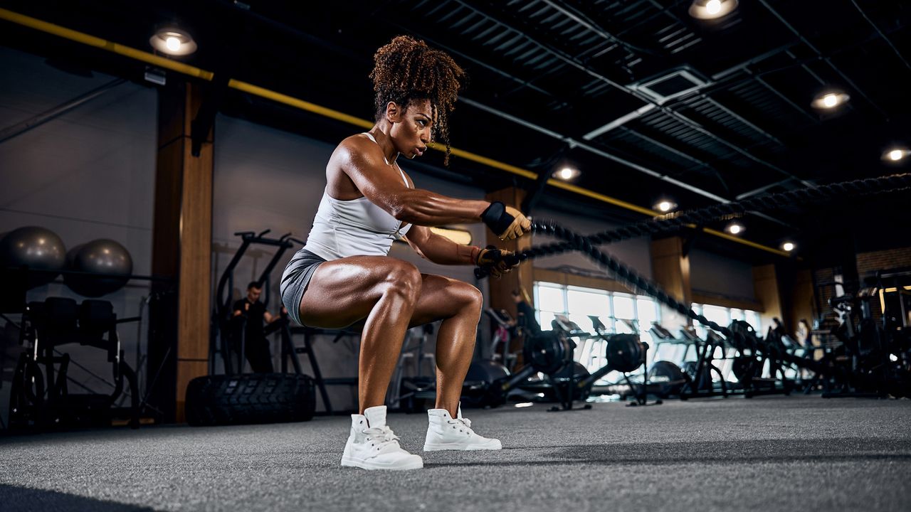 Motivated strong sporty lady performing the alternating waves exercise with battle ropes at the gym