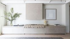 A white living room with a textured rock fireplace, a vase of stems, a stack of books, and a rug