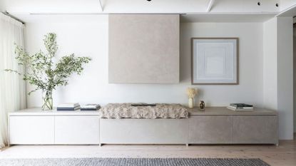 A white living room with a textured rock fireplace, a vase of stems, a stack of books, and a rug