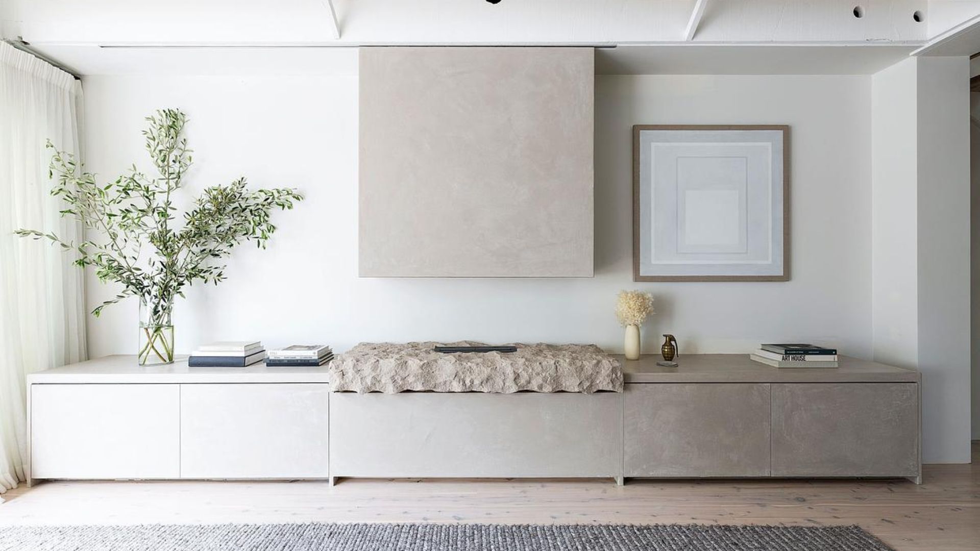 A white living room with a textured rock fireplace, a vase of stems, a stack of books, and a rug