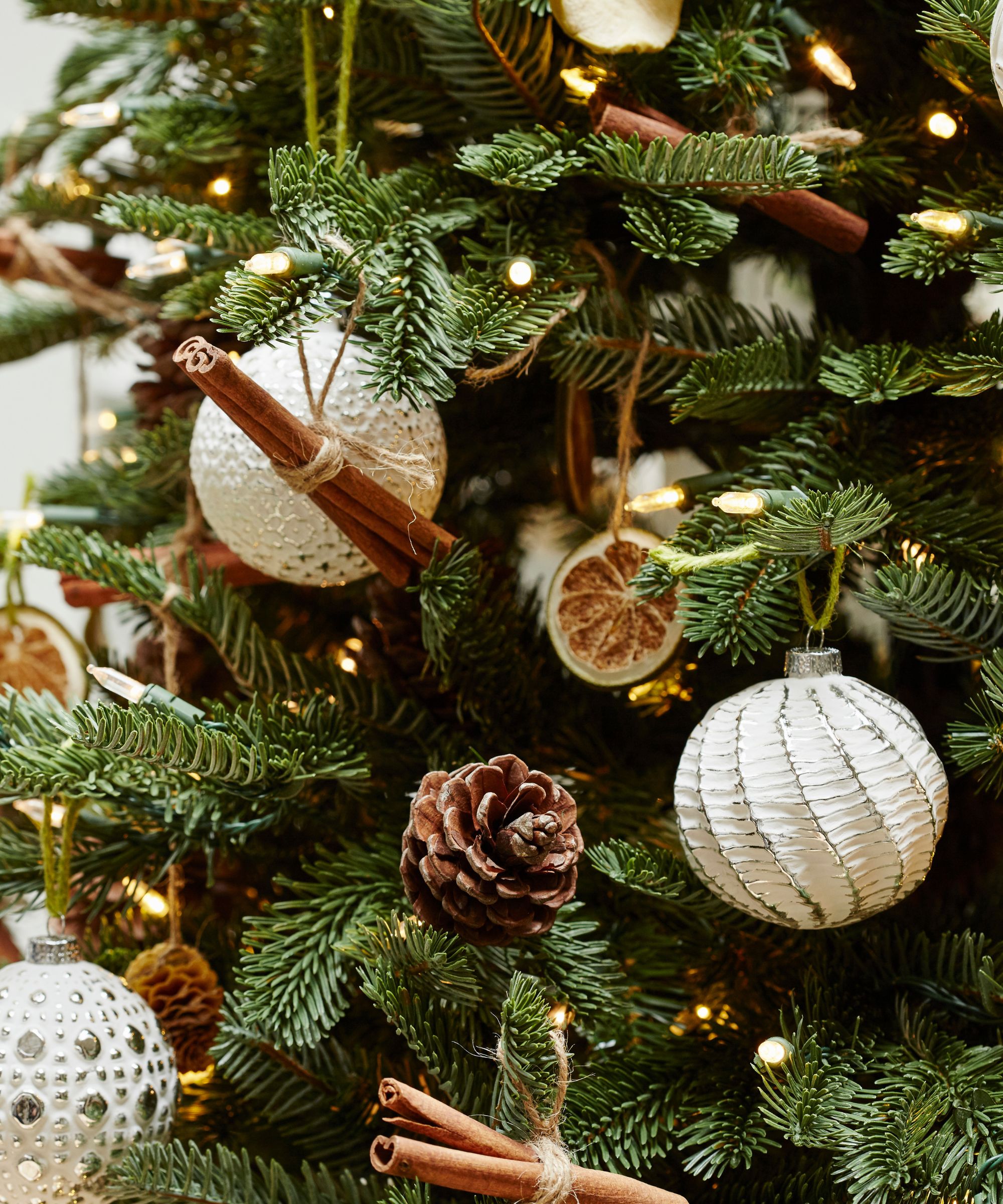 A close-up of a Christmas tree with white baubles, pinecones, and dried fruit and cinnamon sticks