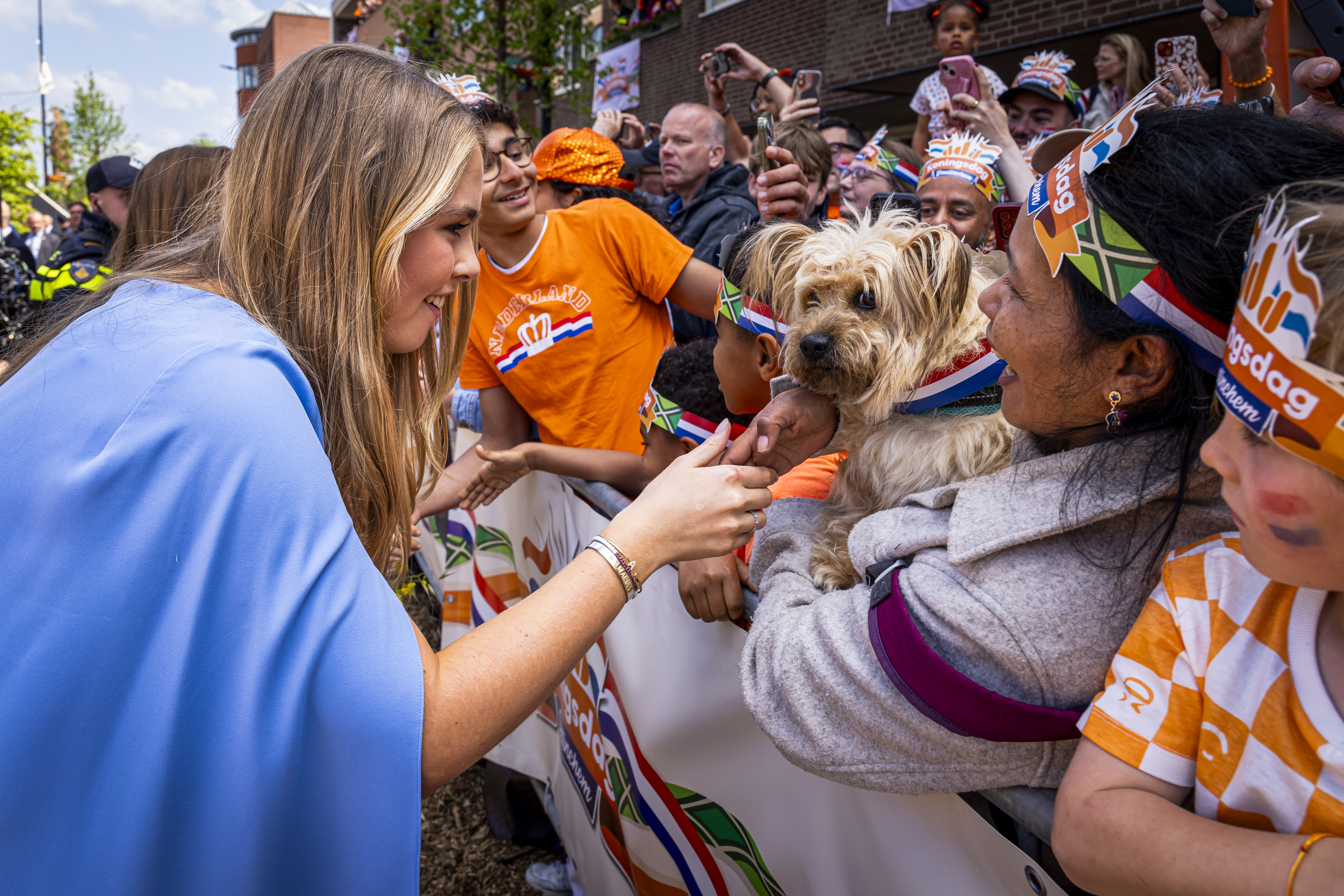 Princess Catharina-Amalia wearing a blue cape dress petting a dog on King's Day