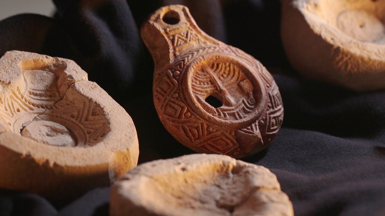 A close-up of a carved clay lamp with other artifacts