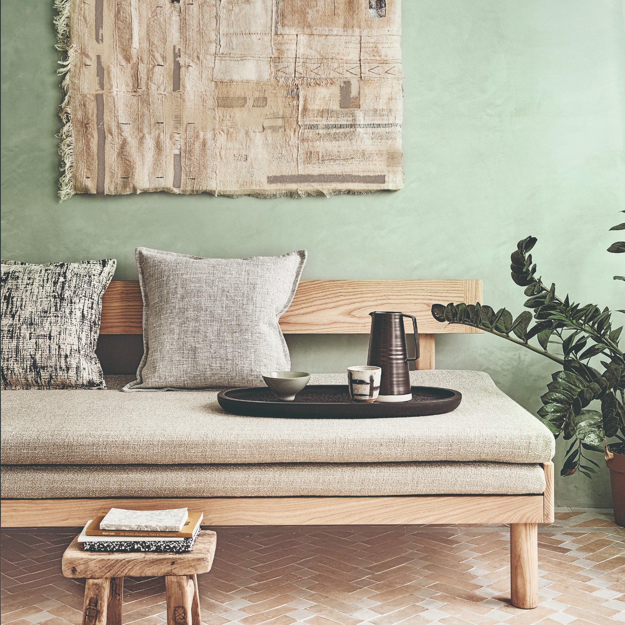 A beige daybed against a light green wall with a beige wall hanging