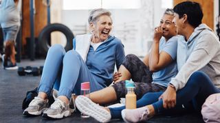 Group of friends laughing together, sitting down on the floor at the gym