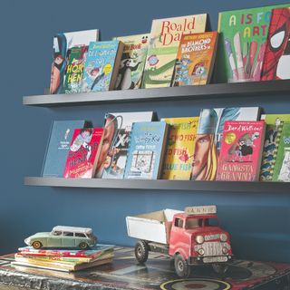 A navy blue-painted children's room with books displayed on two black picture ledges on the wall