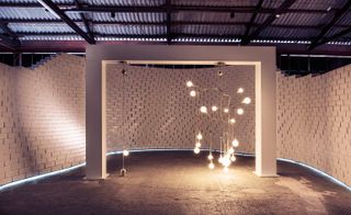 View of a 'The Nature Of Motion’ light installation under a white rectangular arch against a white curved brick wall and dark flooring