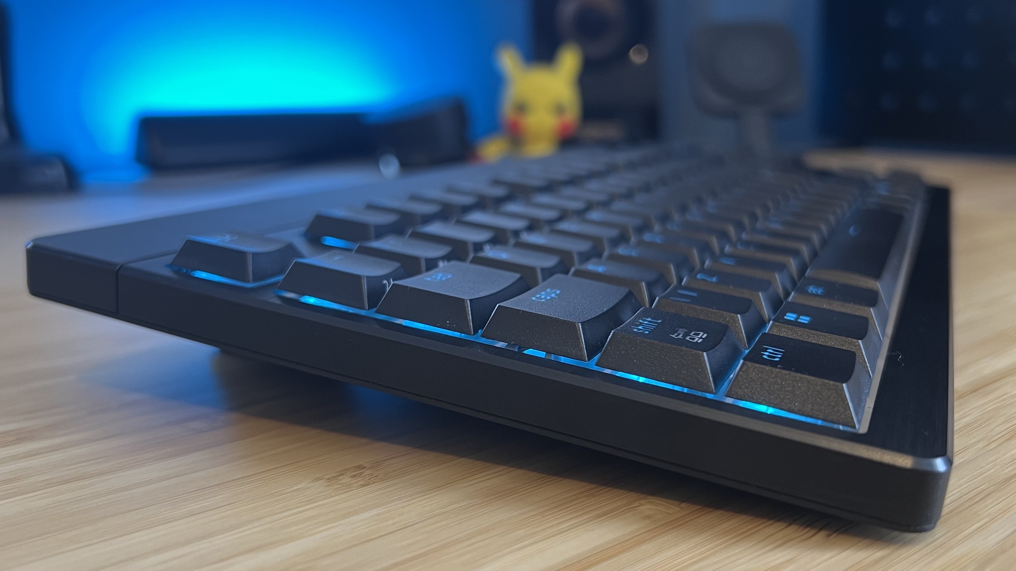 Side view of Razer Blackwidow V4 Low Profile gaming keyboard on a wooden desk with blue backlighting