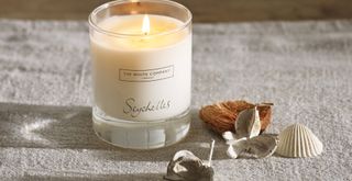 best-selling The White Company seychelles scented candle on a rustic tablecloth next to seashells