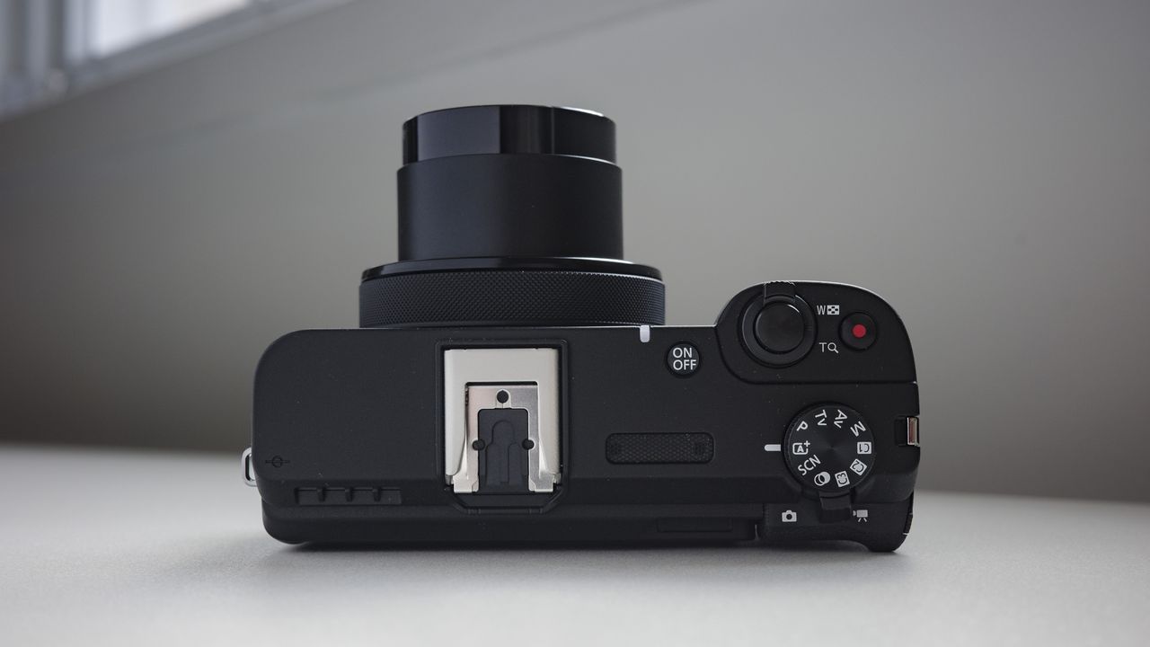 Top plate of the Canon PowerShot V1 compact vlogging camera on a white desk, lens extended