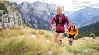 Woman and man running uphill with backpacks on